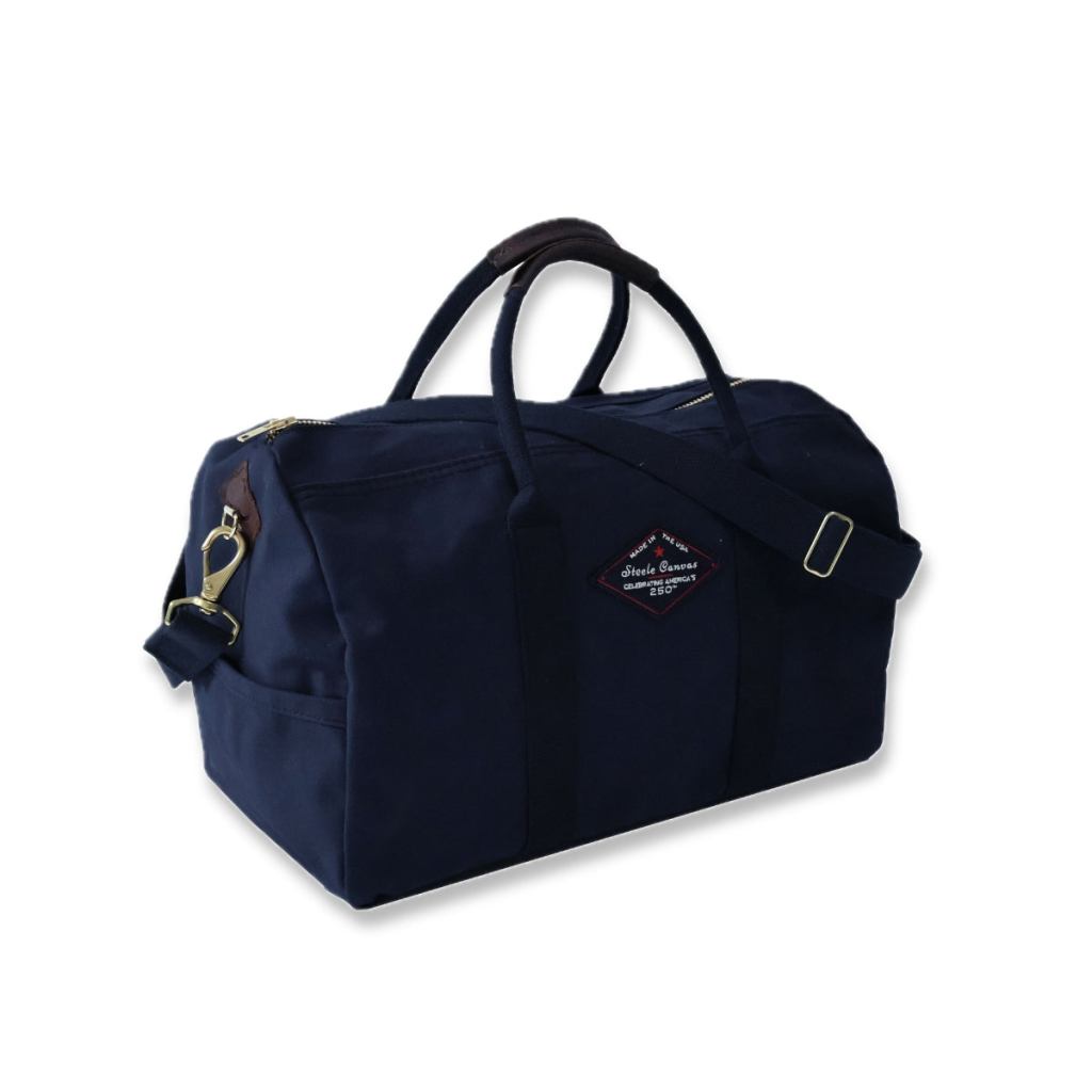 Angled view of a midnight-navy Steele Canvas bag with handles, shoulder strap, and 250th anniversary patch.