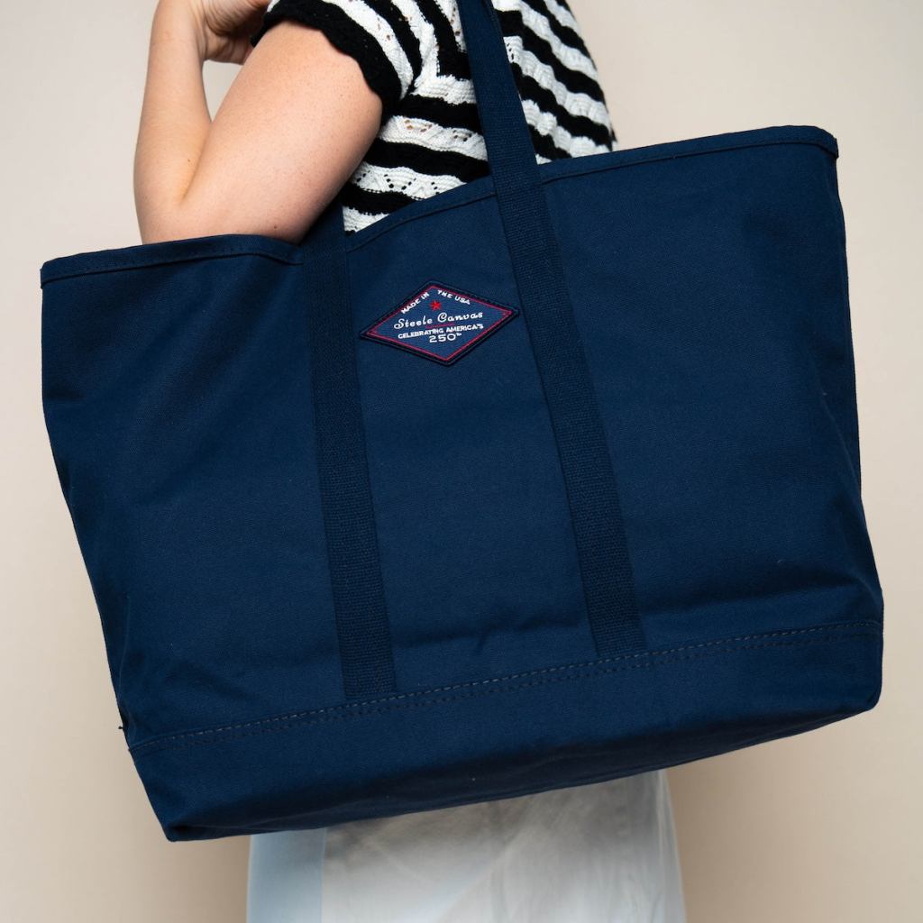Person carrying a large midnight-navy Steele Canvas tote with the 250th anniversary patch.