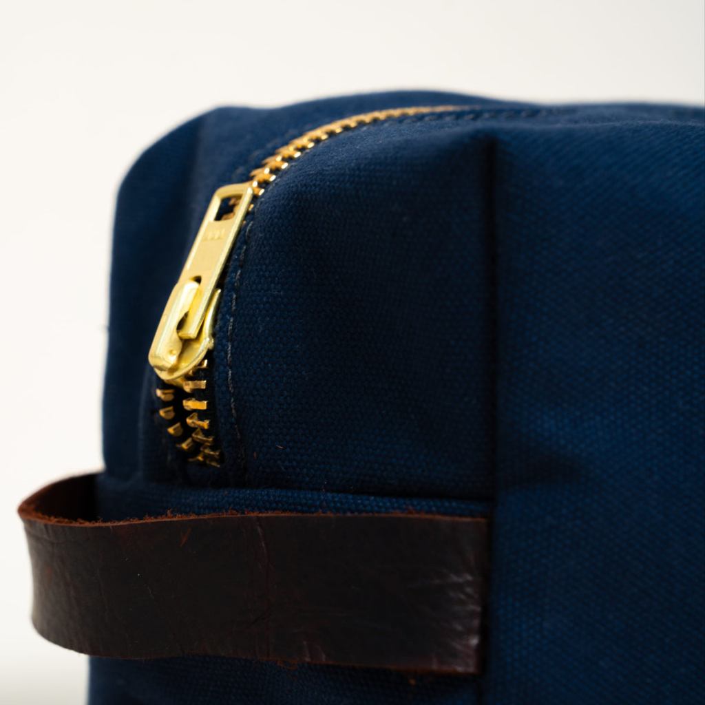 Close-up of the brass zipper and leather handle on a midnight-navy Steele Canvas Dopp kit.