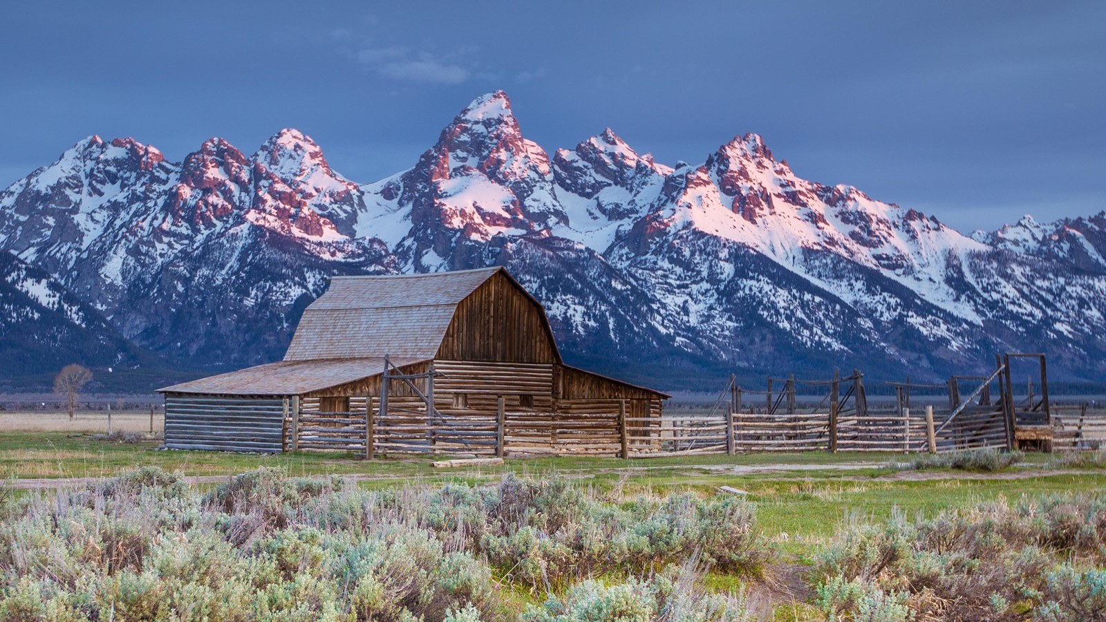 A log barn and wooden corral at Mormon Row beneath the snow-covered Teton Range.
