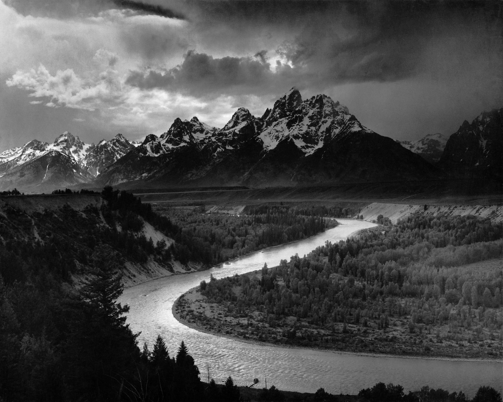 Black-and-white view of the Snake River curving below the Teton Range, with clouds above the mountains.